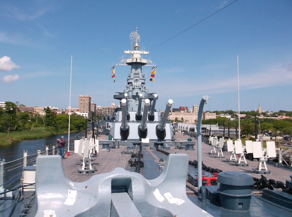 Battleship deck with large gun turrets, city skyline in background.