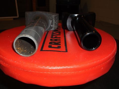 1999 Mercury Grand Marquis - Two driveshaft yokes are shown, one is a rusty metal tube and the other is a shiny black part with splines inside. They are resting on a re…