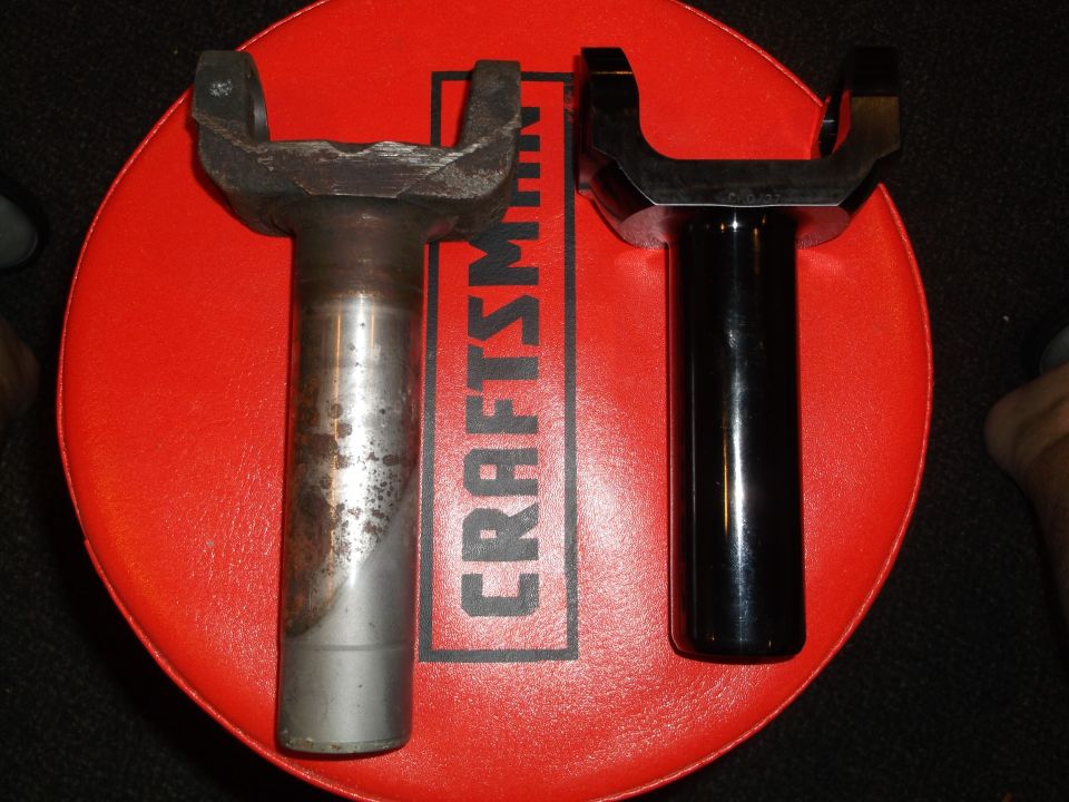 Rusty driveshaft yoke next to a new black driveshaft yoke on a red stool.