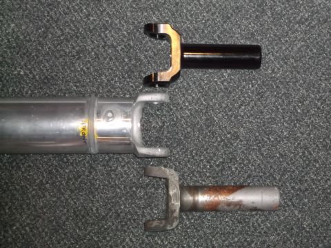 1999 Mercury Grand Marquis - Three driveshaft yokes are shown against a dark carpeted background. The top yoke is black, the middle yoke is silver with yellow writing t…