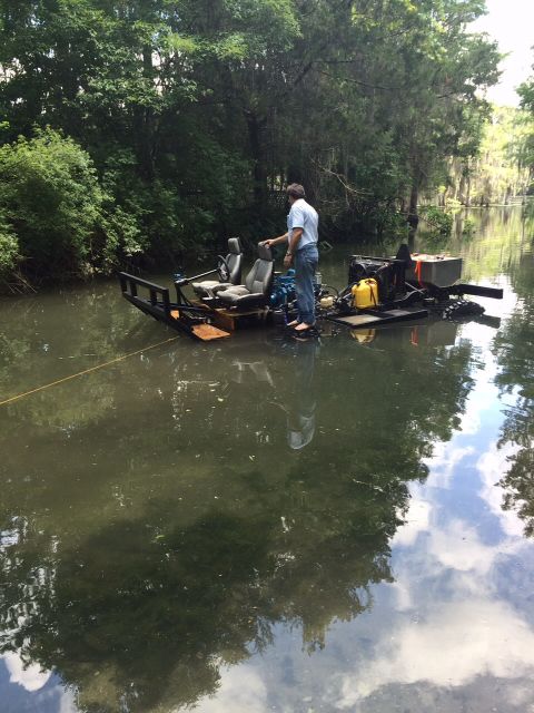 1992 Ford Bronco - A man stands on a custom-built, flat-bottomed watercraft with two seats and a visible engine, navigating a narrow, tree-lined waterway.