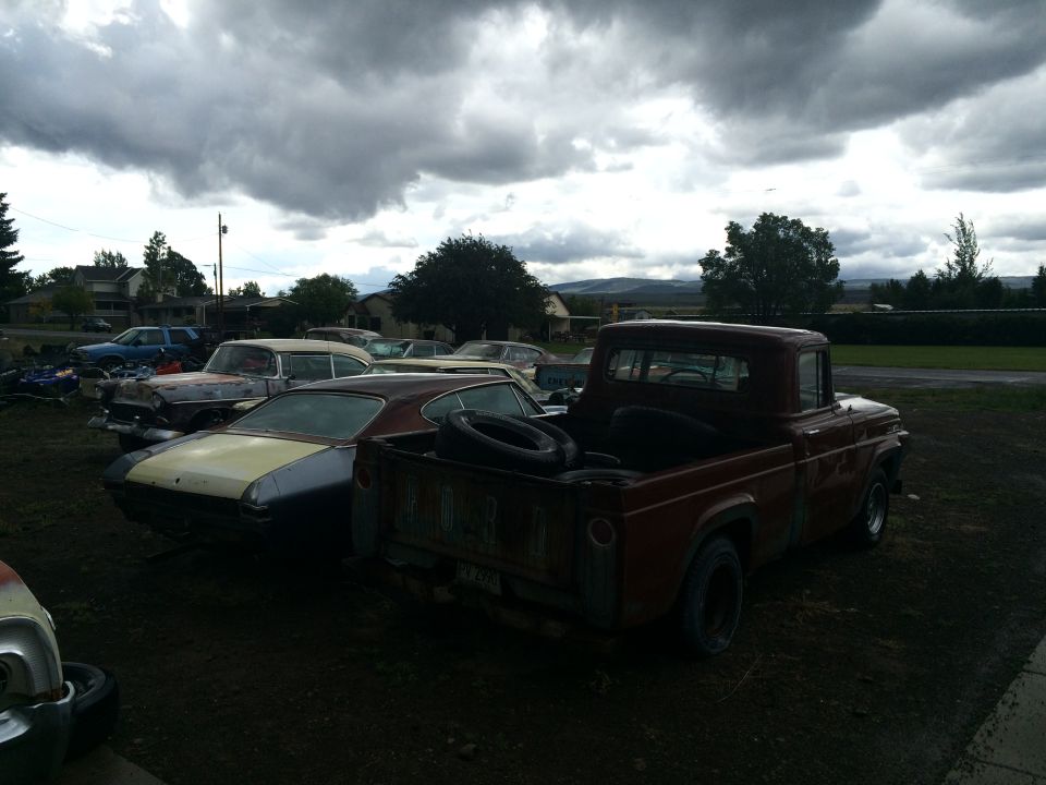 Photo of vintage cars and a Ford pickup in a gravel lot