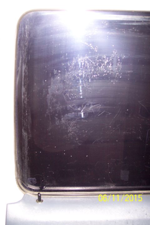 1990 Ford Bronco - A close-up view of the dark tinted rear window of a vehicle, showing numerous scratches and glare from bright light. The date stamp "06/11/…