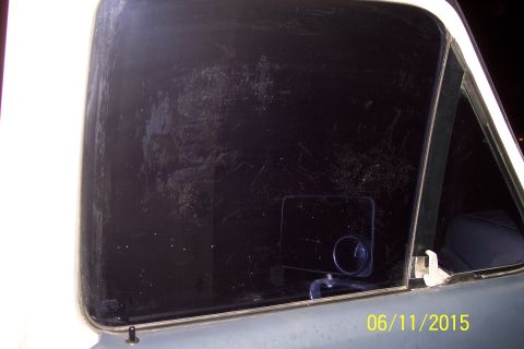 1990 Ford Bronco - The rear passenger side window of a vehicle is shown, heavily scratched and dirty. A small, square side mirror is visible mounted on the in…