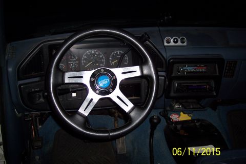 1990 Ford Bronco - The interior of a Ford Bronco shows a custom steering wheel with a Ford logo, aftermarket gauges, and a manual transmission shifter. The da…