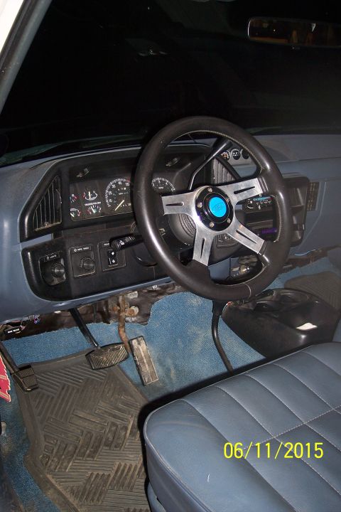 1990 Ford Bronco - The interior of a Ford truck or SUV features a custom steering wheel, dashboard gauges, and blue carpeting. The driver's side pedals and a…