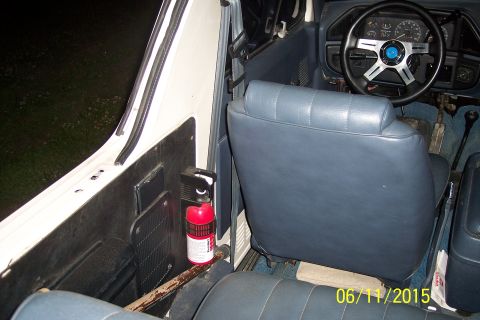 1990 Ford Bronco - Interior view of a vehicle, showing the driver's side door panel with a mounted fire extinguisher and the passenger seat. The dashboard and…