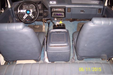 1990 Ford Bronco - The interior of a classic Ford Bronco is shown, featuring blue vinyl seats, a custom steering wheel, and a center console with a radio and…