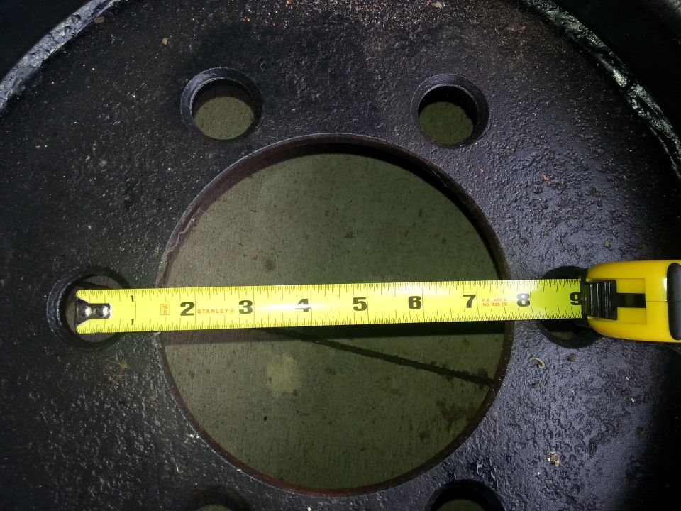 Yellow measuring tape measuring the center hole of a black metal wheel.