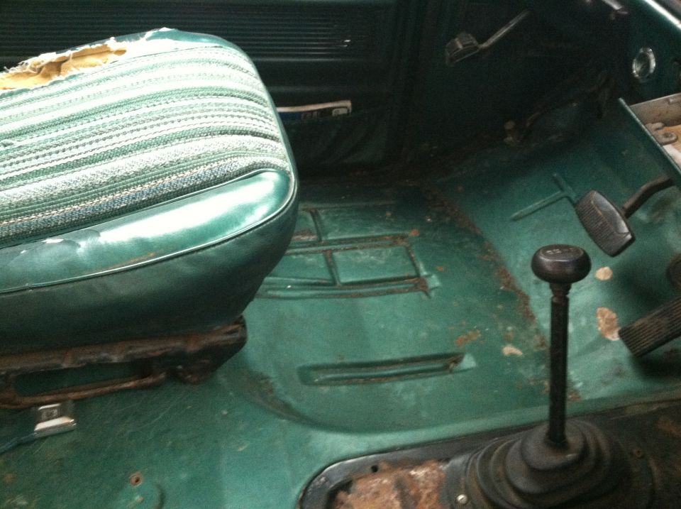 Interior of a vintage vehicle with green seat, floor shifter, and pedals.