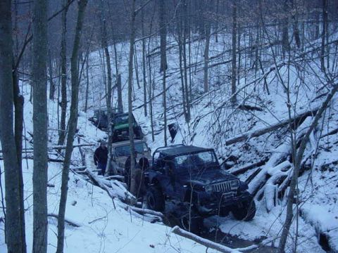 1992 Ford Bronco - Off-road vehicles traverse a snowy forest trail, navigating obstacles and inclines.