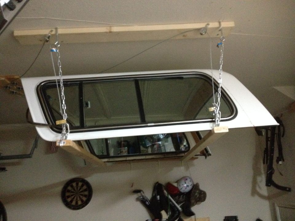 White truck camper shell hanging from garage ceiling by chains and cables attached to a wood board
