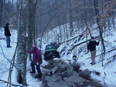 1992 Ford Bronco - Several people observe a green off-road vehicle struggling in a muddy, snow-covered trail.