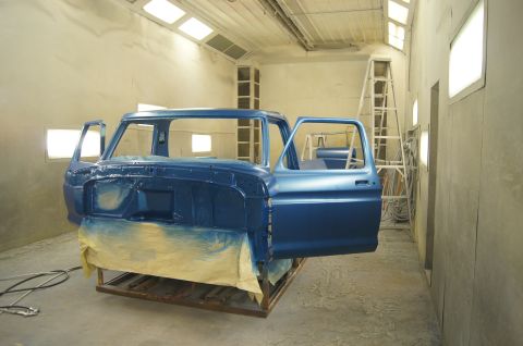 1979 Ford Bronco - A blue truck cab is being prepped for painting inside a spray booth. The doors are open and the front of the cab is covered with masking pa…