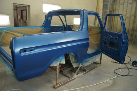 1979 Ford Bronco - The body of a blue pickup truck is shown in a workshop, with the doors open and the bed area covered in protective sheeting. The vehicle is…
