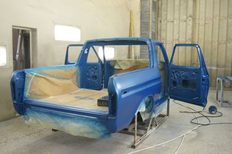 1979 Ford Bronco - The body of a blue Ford Bronco is shown in a paint booth, with doors open and the bed area covered in masking paper. The vehicle is on a st…