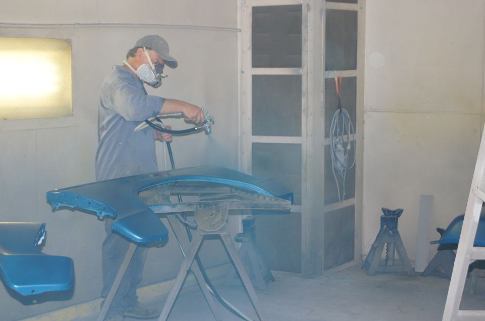 Person in respirator mask spray painting a blue car fender on a stand.