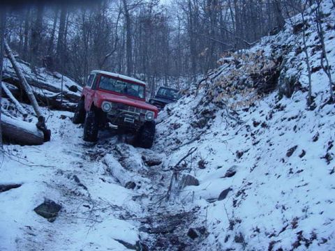 1992 Ford Bronco - A red 1992 Ford Bronco navigates a snowy, wooded trail, with a second vehicle visible in the background.