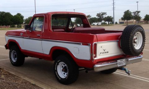 1979 Ford Bronco - The rear passenger side of a red and white 1979 Ford Bronco is shown parked in a paved lot. A spare tire is mounted on the back, and a trai…
