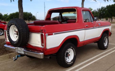 1979 Ford Bronco - The rear passenger side of a red and white two-tone Ford Bronco is shown parked in a lot. A spare tire is mounted on the rear, and the vehi…