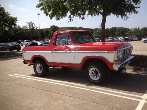 1979 Ford Bronco - A red and white 1979 Ford Bronco is parked in a lot under a tree. The vehicle has a spare tire mounted in the bed.