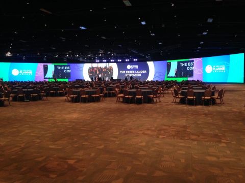 1987 Suzuki Samurai - A large conference hall is set up with round tables and chairs facing a massive curved LED screen displaying event graphics and text. The s…