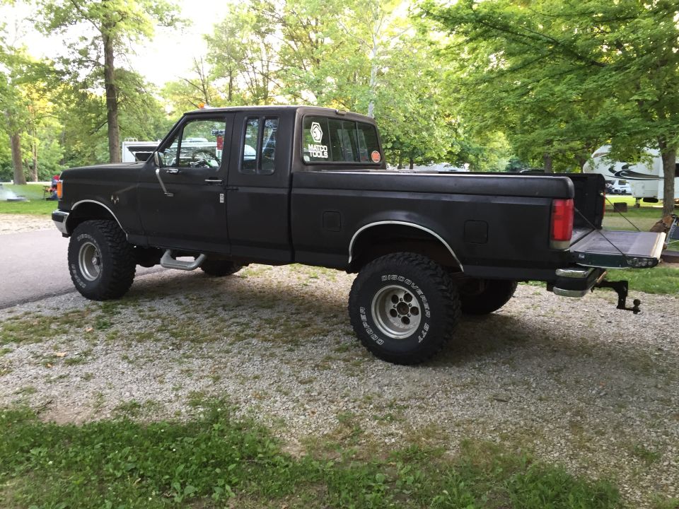 Black lifted Ford F-150 pickup truck with tailgate down, parked on gravel.