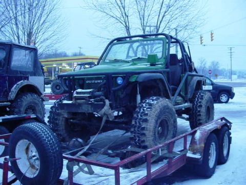 1992 Ford Bronco - A modified green Suzuki Samurai is loaded onto a trailer in a snowy outdoor setting.