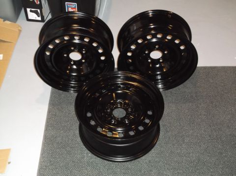 1999 Mercury Grand Marquis - Three black steel wheels are arranged in a cluster on a gray carpeted surface. The wheels have multiple circular cutouts and appear to be f…