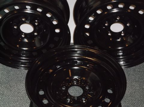 1999 Mercury Grand Marquis - Four black steel wheels are arranged on a gray carpeted surface. The wheels have a glossy finish and visible bolt holes around the center h…