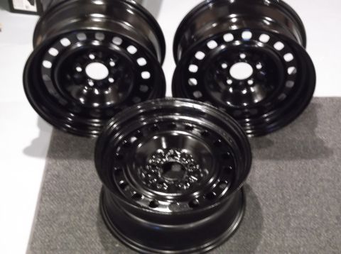 1999 Mercury Grand Marquis - Three black steel wheels are arranged on a gray surface. The wheels are facing the camera at different angles, with the closest one centere…