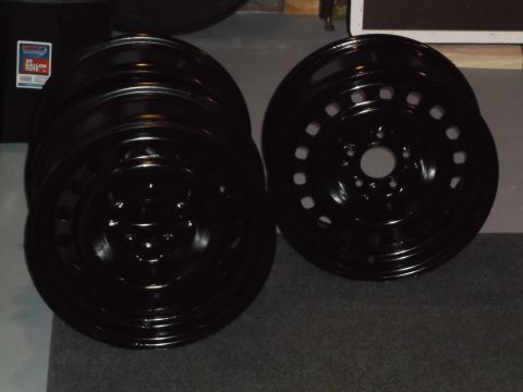 1999 Mercury Grand Marquis - A stack of four black steel wheels is shown in the foreground, with a fifth wheel visible to the right. A black storage tote with a label i…
