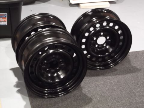 1999 Mercury Grand Marquis - Two black steel wheels are stacked on top of each other, with one wheel slightly offset to the right. The wheels have a simple design with…
