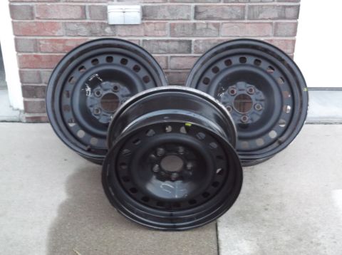 1999 Mercury Grand Marquis - Three black steel wheels are arranged in a cluster in front of a brick wall. One wheel is in the foreground, facing the camera, while two o…