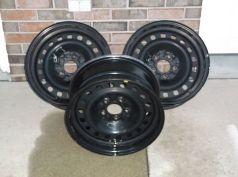 1999 Mercury Grand Marquis - Three black steel wheels are arranged in a triangular pattern against a brick wall. One wheel is in the foreground, slightly angled, with t…