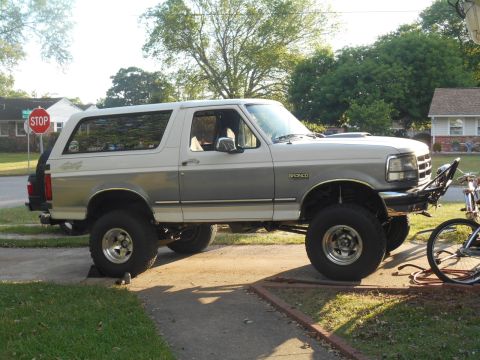 1994 Ford Bronco - A lifted two-tone white and gray 1994 Ford Bronco is parked on a driveway with a stop sign visible in the background. The vehicle has after…