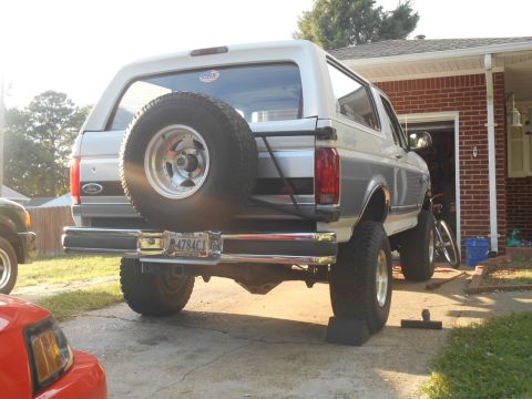 1994 Ford Bronco - Rear quarter of a lifted two-tone Ford Bronco with rear-mounted spare tire parked in a driveway.