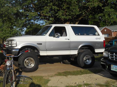 1994 Ford Bronco - A lifted white and silver two-door Ford Bronco is parked on a dirt lot with a bicycle in the foreground. The vehicle has large off-road tir…