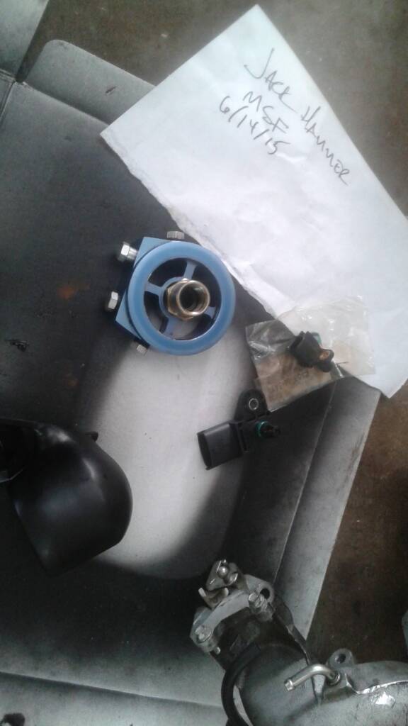 Blue oil filter housing adapter and black sensor next to paper with text.