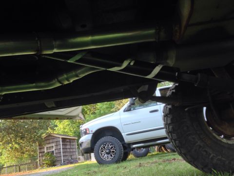 1979 Ford Bronco - The underside of a vehicle is visible, with a white pickup truck parked in the background.