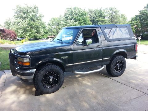 1994 Ford Bronco - This black Ford Bronco is shown from the side with a soft top and custom wheels.