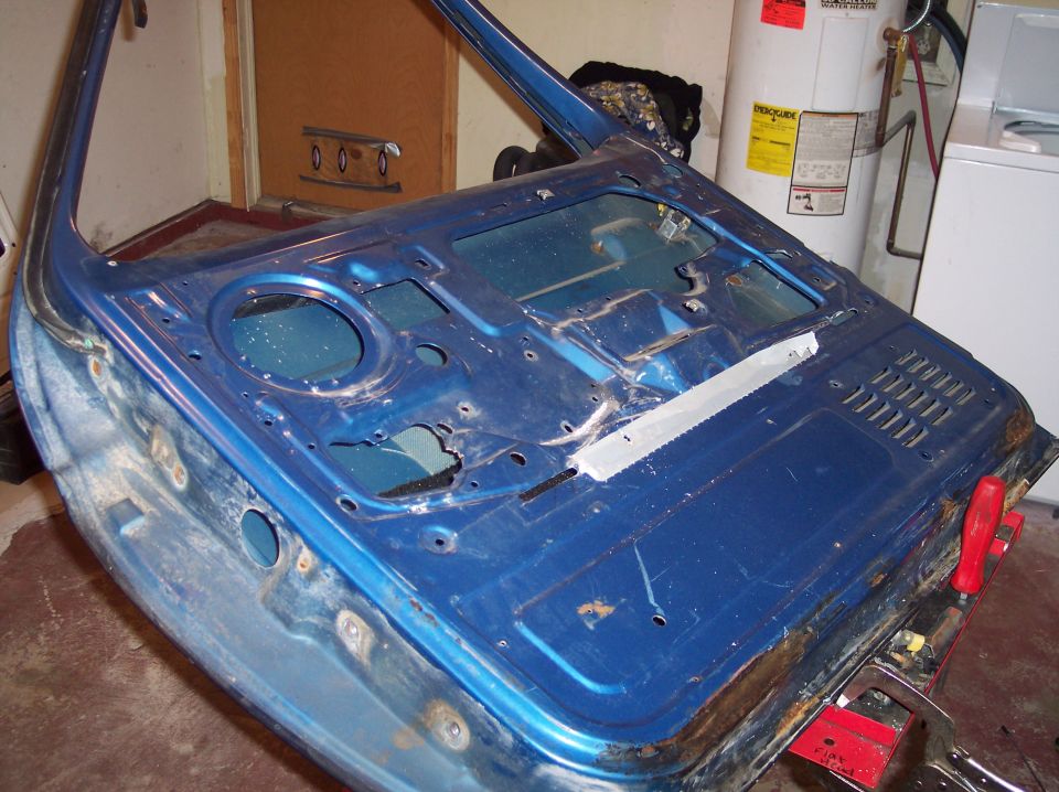Blue car door, stripped down, showing interior metalwork and some rust around the edges. It's in a garage with a water heater and washing machine in the background