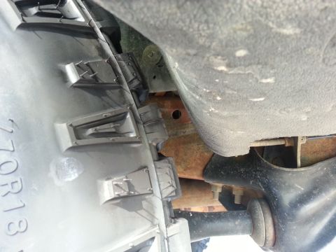 1994 Ford Bronco - Close-up of the undercarriage reveals rusty metal components and a partial plastic trim piece with identifying numbers.