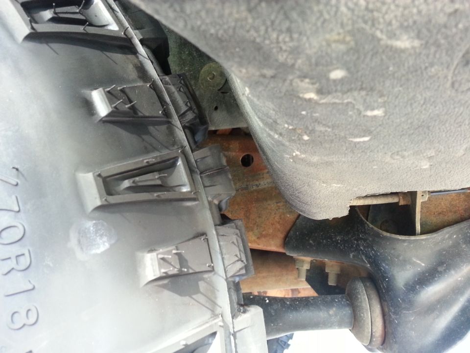 Underside view of vehicle chassis with visible rust and suspension components. Part of a black plastic trim piece with numbers '270R13' is visible