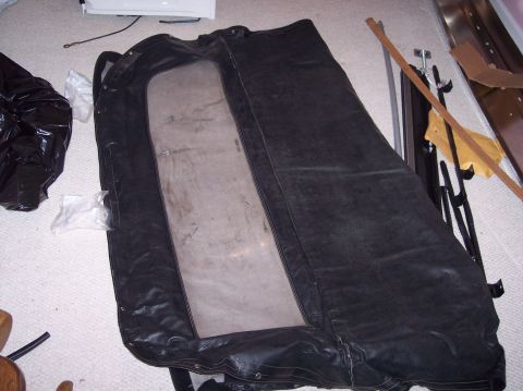 1990 Ford Bronco - A black soft-top with a clear window is spread out on a carpeted surface, with various items in the background.