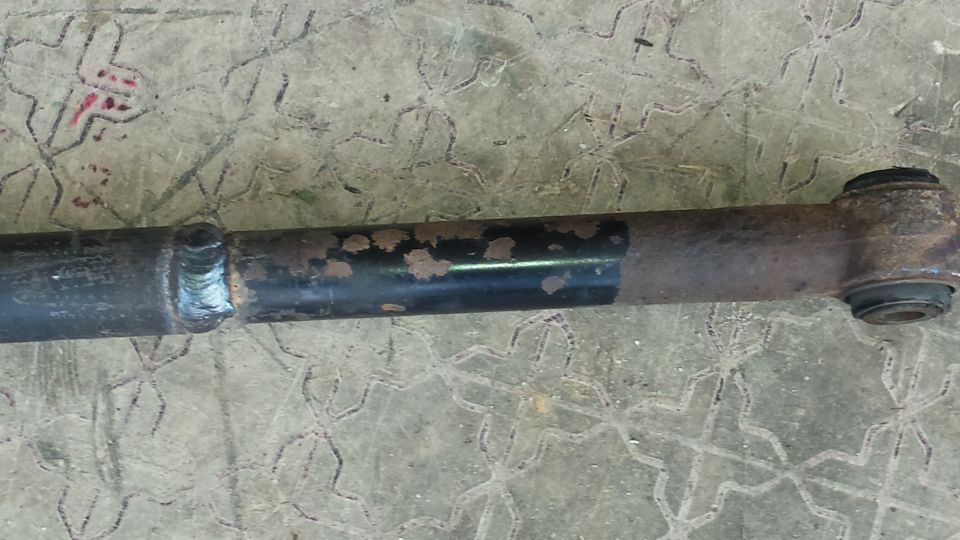 Rusty suspension part with a weld and rubber bushing, on a textured surface