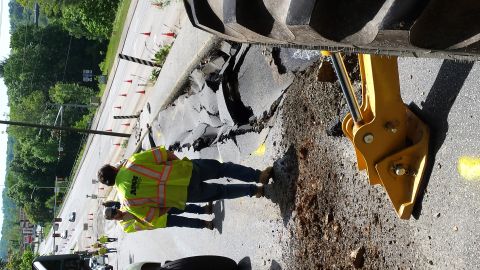 1979 Ford Bronco - Workers are assessing damage to a road that has collapsed, with heavy machinery present.