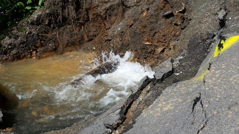 1979 Ford Bronco - A section of road has collapsed, with water flowing through the debris and a yellow line marking the edge.