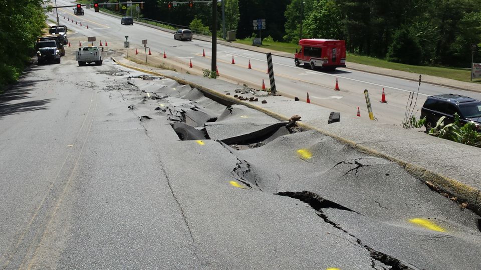 Road collapsed with debris, traffic cones, and vehicles on the side