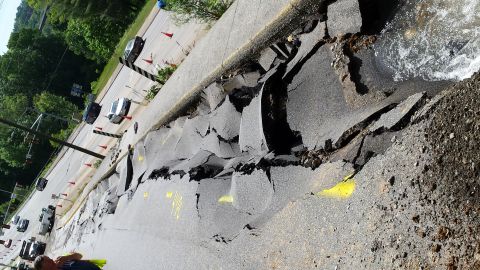 1979 Ford Bronco - A section of road has collapsed, with water flowing into the gap. Several cars are visible on the remaining road surface.
